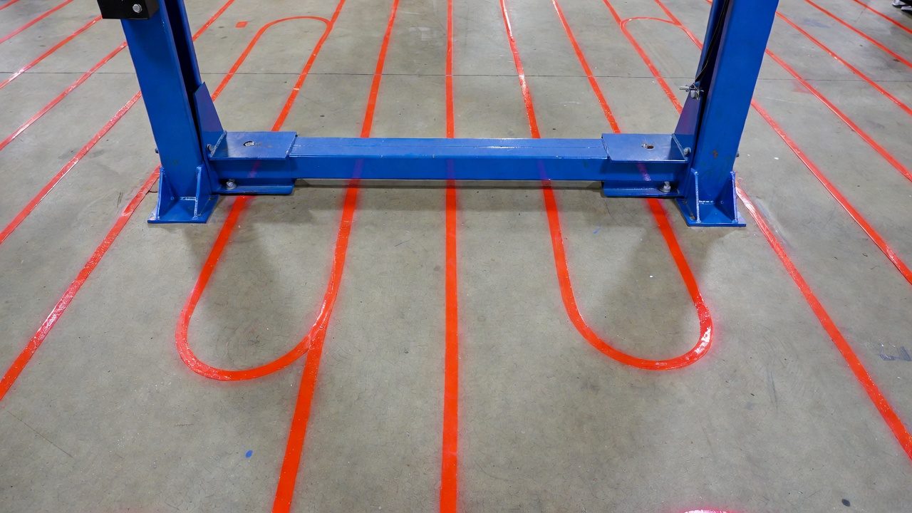 Red layout marks showing radiant heating lines under a vehicle lift